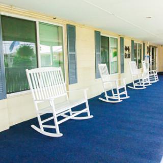 A serene porch featuring white rocking chairs on a blue carpet, inviting relaxation.