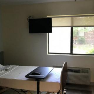 A hospital room with a bed, tray table, and television.