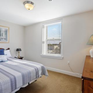 A tidy bedroom with a bed, dresser, and window with blinds.