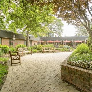A peaceful courtyard with benches, trees, and a paved pathway surrounded by lush landscaping.