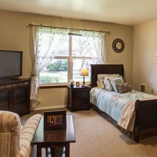 A cozy bedroom with a single bed, a large window, and a television.