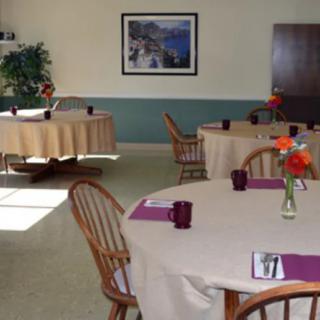 A neatly arranged dining room with round tables set for a meal, featuring floral centerpieces and wooden chairs.