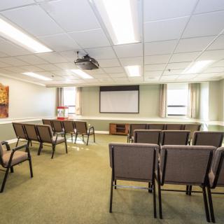 A meeting room with a projector screen and arranged chairs, ready for a conference or presentation.