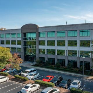 A modern office building with ample parking, reflecting a clear sky.