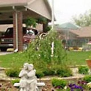 A garden scene with a statue, plants, and a house in the background.