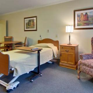 A hospital room with a bed, side table, chair, and lamp.