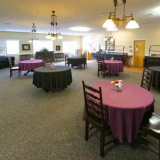A spacious dining area with round tables and wooden chairs, featuring chandeliers for lighting.