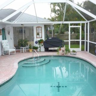 A cozy backyard with a screened pool and patio area, featuring outdoor furniture and plants.