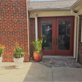 A house entrance featuring a brick wall, glass double doors, and potted plants.