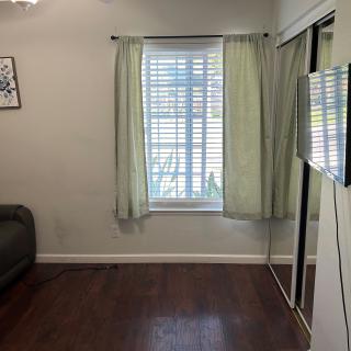 A cozy living room with a window, curtains, sofa, and wall-mounted television.