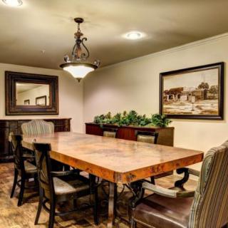 A cozy dining room with a large wooden table surrounded by chairs, featuring a chandelier and decorative elements like a painting and a mirror.