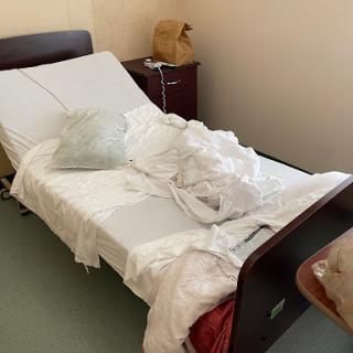 A disheveled hospital bed with crumpled linen in a care room.