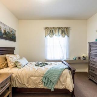 A cozy bedroom with a neatly made bed, wooden furniture, and soft natural lighting.