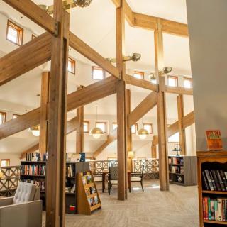 A cozy library interior with wooden beams and ample natural light filtering in through large windows.