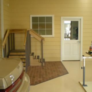Interior view of a garage with a car parked, stairs leading to a door, and a window on the wall.