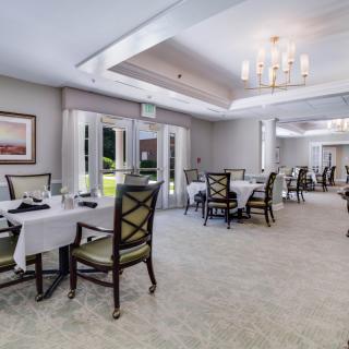 An elegant dining room with neatly arranged tables and chairs, illuminated by natural light and a chandelier.