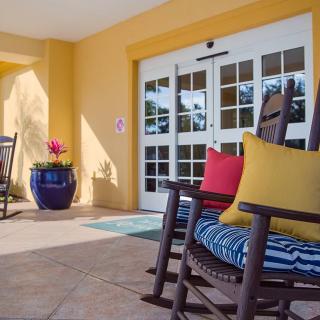 A cozy patio setting with a rocking chair and colorful cushions in front of an entrance with glass doors.