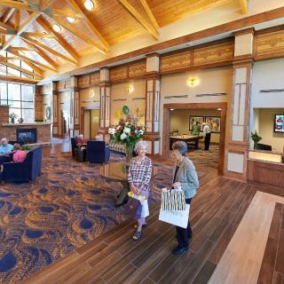 A spacious lobby with wooden ceilings, comfortable seating, and two people walking with shopping bags.