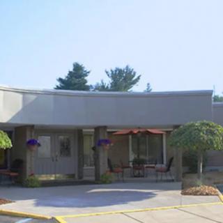 A modern building with a patio area, featuring outdoor seating and surrounded by trees on a sunny day.