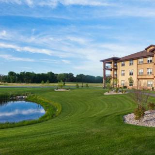A scenic view of a building by a pond with lush greenery and a clear blue sky.