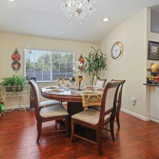 A cozy dining room with a wooden table and chairs, illuminated by a chandelier and decorated with plants and wall art.