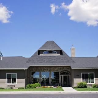 A modern house with a distinctive roof, set against a clear blue sky with scattered clouds.