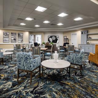 A modern lobby featuring a seating area with patterned chairs, round tables, and decorative elements on a carpeted floor.