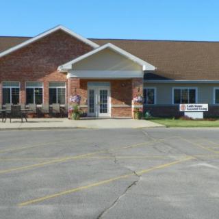 A brick commercial building with a main entrance and an adjacent parking lot under a clear blue sky.
