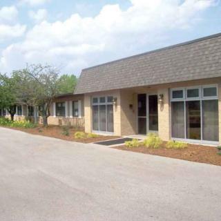 A view of a building with large windows, adjacent to a road lined with trees under a partly cloudy sky.