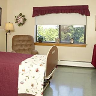 A hospital room with a bed, chair, and window.