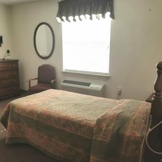 A cozy bedroom with a bed, dresser, chair, and window.