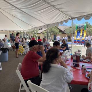 A lively outdoor gathering under a tent, filled with families enjoying food and festivities.