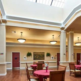 A well-lit dining area with round tables and chairs, featuring a skylight and elegant columns.