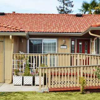 A quaint house with a red-tiled roof and wooden deck surrounded by a neatly kept front yard.
