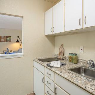 A compact kitchen with white cabinets and a granite countertop, featuring a double sink.