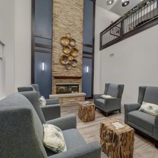 A modern lounge area featuring comfortable seating around a central fireplace with wood accents and high ceilings.