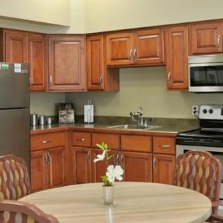 A modern kitchen with wooden cabinets, a stainless steel refrigerator and oven, and a round dining table adorned with flowers.