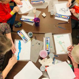 Children engaged in watercolor painting around a table.