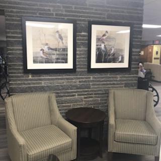 A cozy seating area featuring two striped chairs, a small table, and framed artwork on a stone wall.
