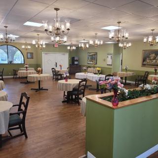 A spacious and elegantly designed dining area featuring multiple tables and chairs, adorned with chandeliers and green accents.