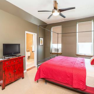 A cozy bedroom features a canopy bed with red bedding, a red dresser with a TV, and a ceiling fan.