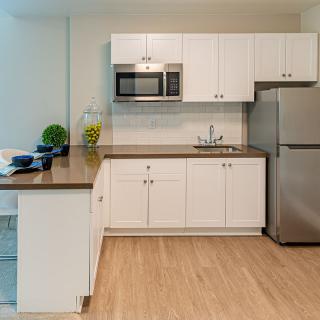 A modern kitchen with white cabinets, a stainless steel refrigerator, and a microwave.