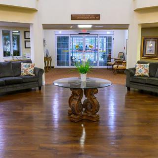 A spacious and well-decorated lobby area featuring two sofas, a central wooden table with a plant, and elegant wood flooring.