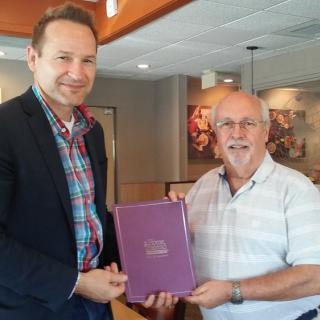 Two men standing inside a room, holding a book and smiling.