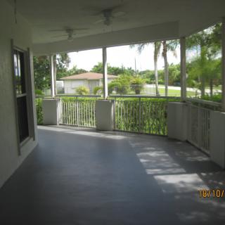 A spacious covered porch with railings, offering a view of tropical palm trees.