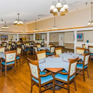 A spacious dining room with neatly arranged tables and chairs, featuring chandeliers and a wooden floor.