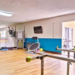 A well-lit exercise room equipped with various gym and rehabilitation tools, including a stationary bike and parallel bars.
