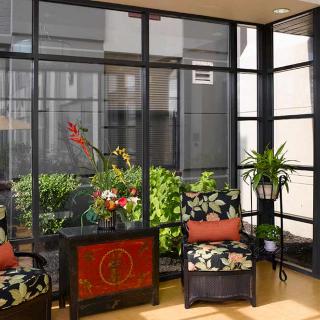 A sunlit room with comfortable chairs and vibrant plants by large windows.