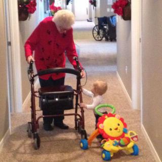 An elderly person using a walker and a child with a toy sharing a moment in the hallway.