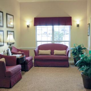 A cozy living room with maroon sofas and armchairs, soft lighting, and decorative plants.